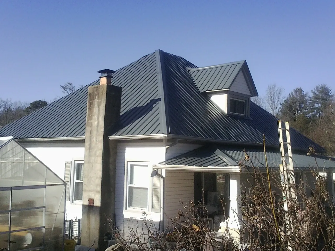 Dark blue standing seam metal roof on a white farmhouse with dormer — Slate & Tile Roof Repair by Roofing Brothers in Marbury