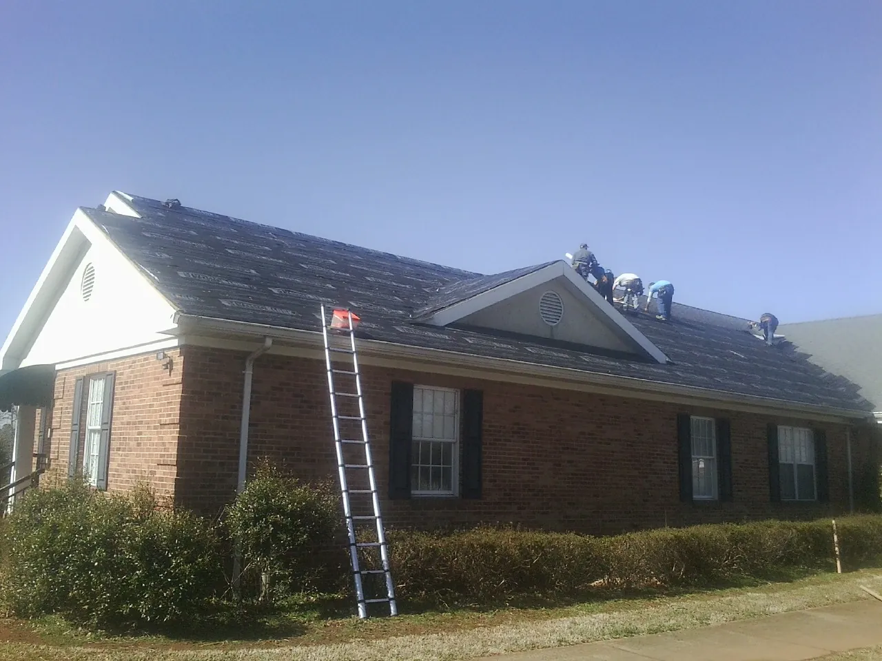 Crew tearing shingles off a brick ranch roof with a ladder set — Metal Roof Repair work by our crew in Marbury
