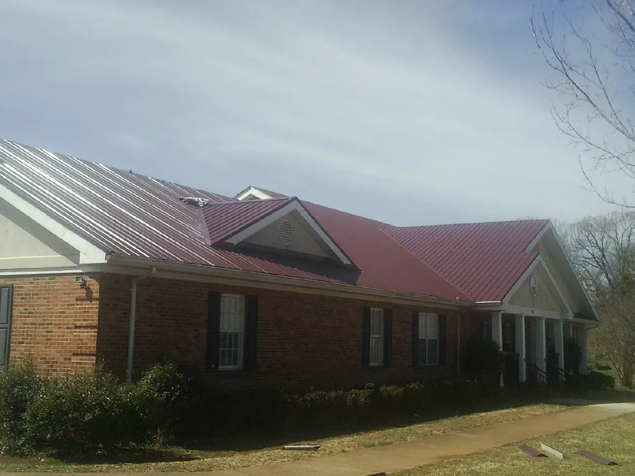 Red metal roof with gabled entries on a long brick building, from a Hail Damage Roof Repair job in Marbury