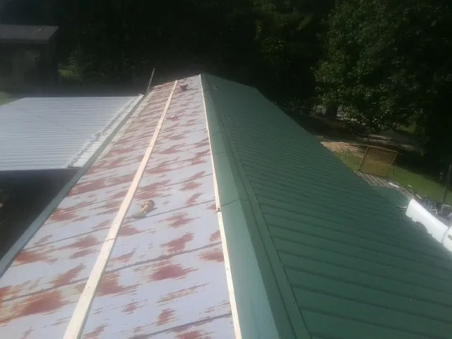 Old rusted panels beside newly installed green metal roofing — Wind Damage Roof Repair by Roofing Brothers in Marbury