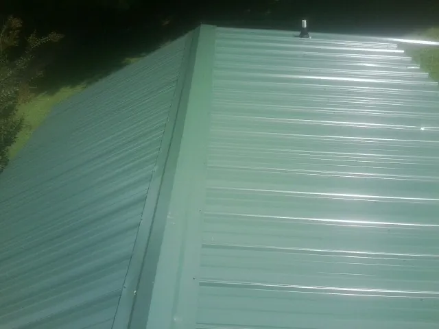 New green metal panels meeting at the ridge of a roof — Flat Roof Repair work by our crew in Marbury