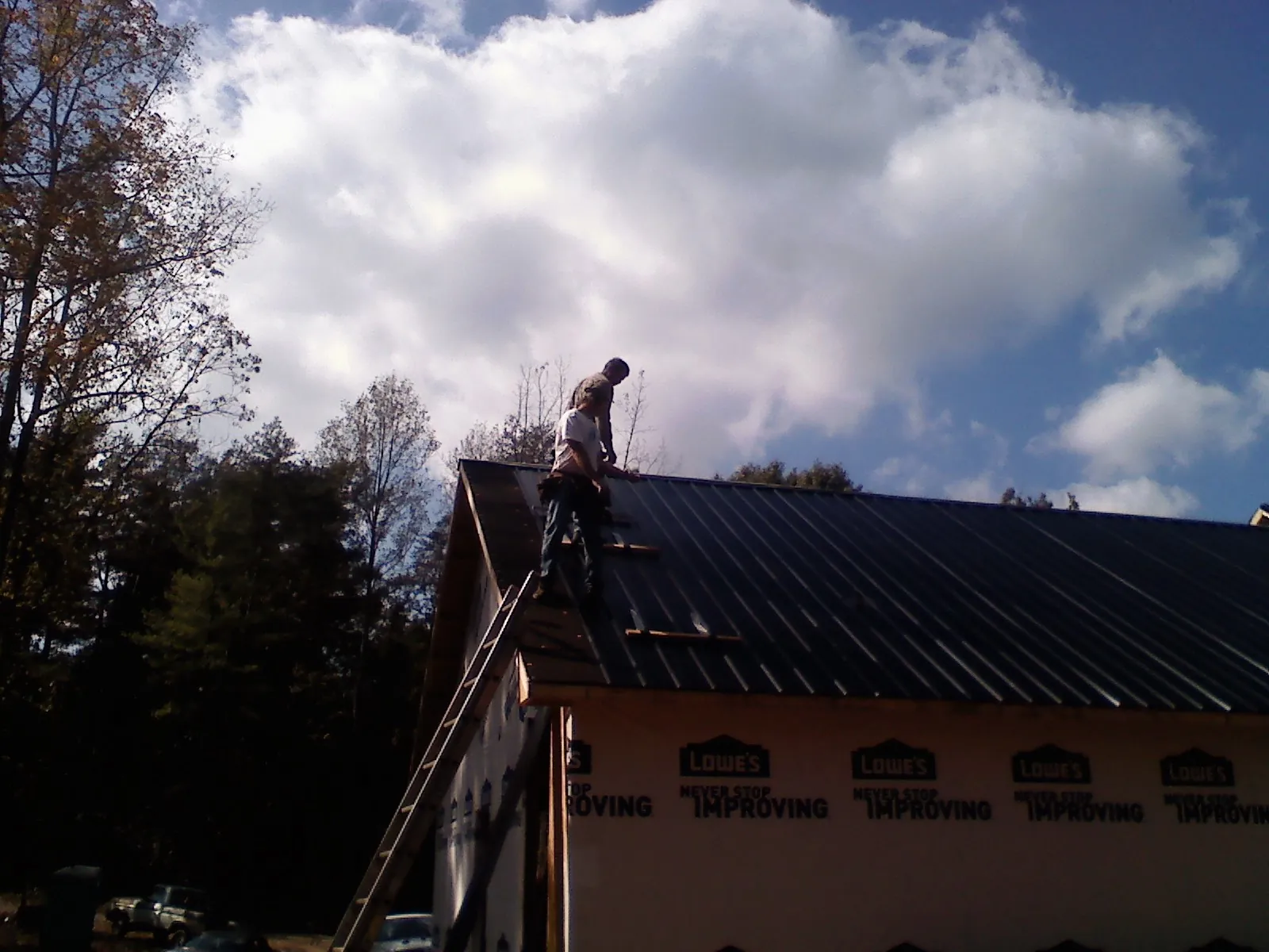 Roofer fastening dark metal panels high against a cloudy sky, from a Roof Inspection job in Marbury
