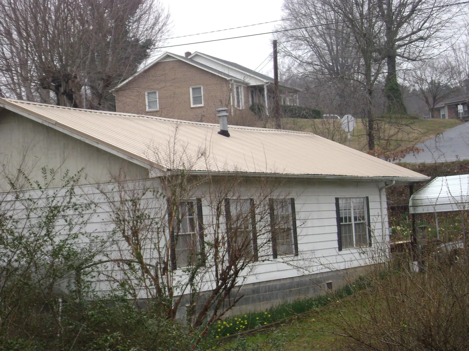 Tan metal roof on a white sided house set into a hillside — Commercial Roofing by Roofing Brothers in Marbury